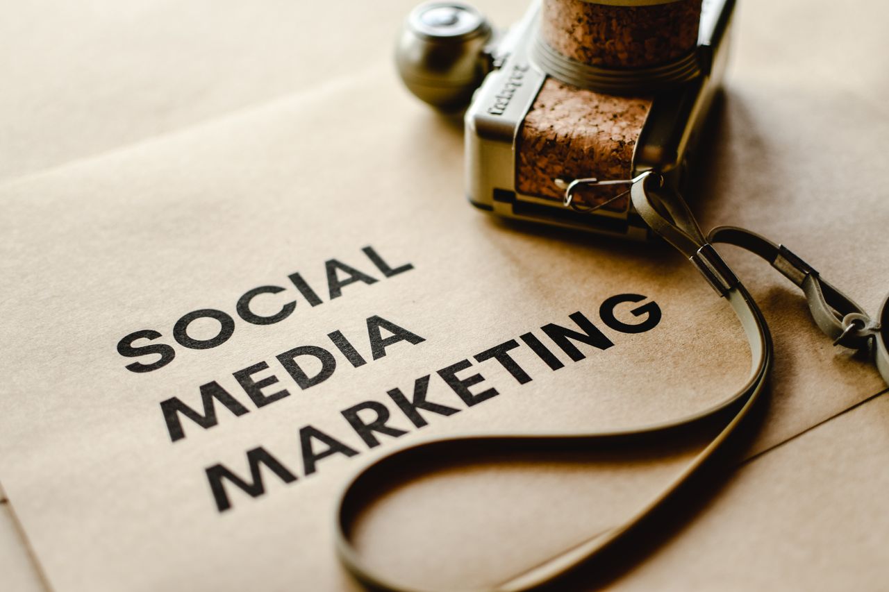 creative-03 Close-up of a camera placed on brown paper with Social Media Marketing text, emphasizing digital marketing themes.